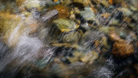 Rocky bottom of mountain river through the clear water, selective focus, blurring the image. Cristal...