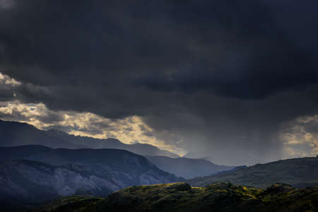 Dramatic dark clouds in mountains before storm. Landscape with mountain range, rain clouds and rays...