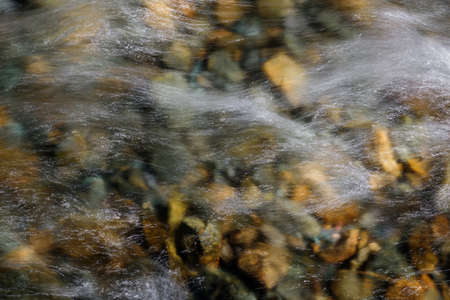 Rocky bottom of mountain river through the clear water, selective focus, blurring the image. Cristal...