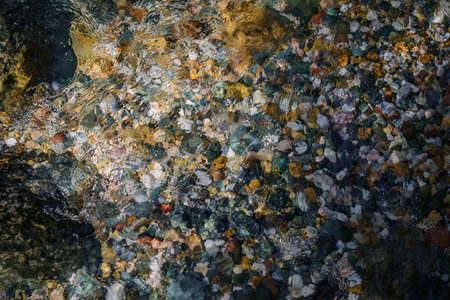 Rocky bottom of mountain stream, close-up. Colorful stones under clear water. Beautiful distortion...