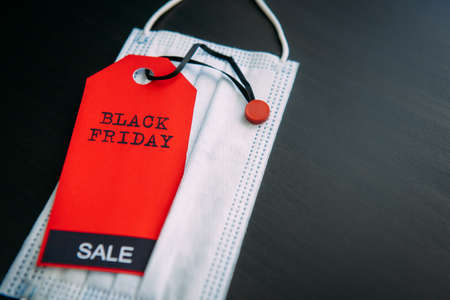 Red tag with the inscription Black Friday on the background of medical mask. Sales in the context of...