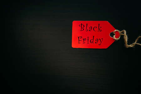 Black friday shopping sale concept. Text on red tag on black wooden background in sunlight. Copy space.の写真素材