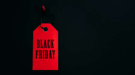Black friday shopping sale concept. Text on red tag on black wooden background. Copy space.