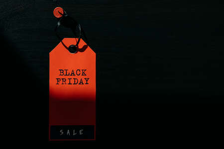 Concept image of label with inscription on dark wooden background, combination of light and shadow. Red tag Black Friday, close-up, copy space.の写真素材