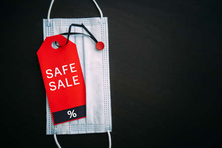 Red tag with the inscription Black Friday on the background of medical mask. Sales in the context of Covid-19 pandemic. Concept of safe shopping.の写真素材