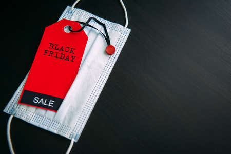 Red tag with the inscription Black Friday on the background of medical mask. Sales in the context of Covid-19 pandemic. Concept of safe shopping.の写真素材