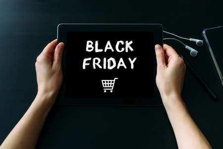 Women's hands holding tablet computer with inscription on screen, dark background, close up. Black friday concept.の写真素材