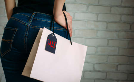 Woman holding a paper bag with tag black Friday. Back view of slender female butt in blue jeans....