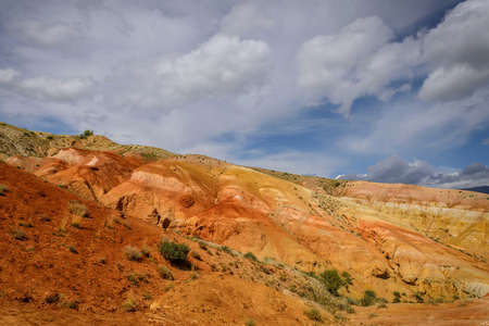 Martian landscape, natural landmark of Altai Republic. Mountains colored red, yellow, and orange against a blue sky with white clouds.の写真素材