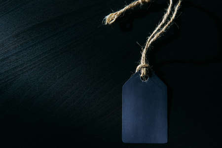 Concept of Black Friday. Empty label on a rope with space for text on black wooden background in sunlight.の写真素材