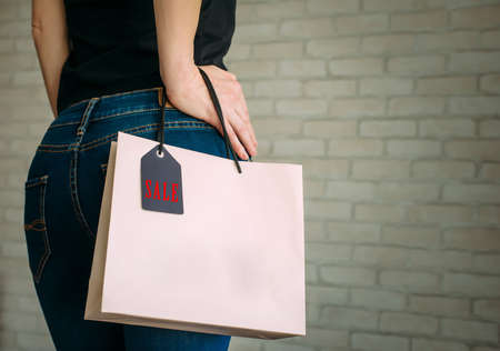 Woman holding a paper bag with tag black Friday. Back view of slender female butt in blue jeans. Concept of shopping, seasonal discounts.の写真素材