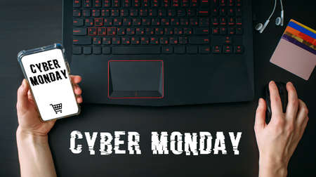 Woman's hands using laptop and smartphone for shopping online at home while Cyber Monday Sales. Top view of the workspace on black background. Promotion inscription on screen.の写真素材
