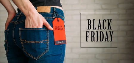 Cropped view slim woman in jeans with label black friday, copy space. Female hands in the back pocket of blue denim pants, close up. Advertising signs.の写真素材