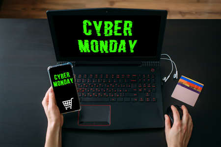 Woman's hands using laptop and smartphone for shopping online at home while Cyber Monday Sales. Top view of the workspace on black background. Promotion inscription on screen.の写真素材