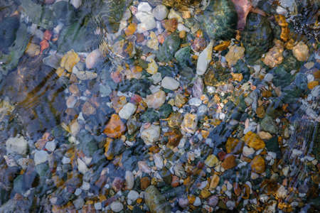 Rocky bottom of mountain stream, close-up. Colorful stones under clear water. Beautiful distortion background. Natural mosaic of small stones. Image for ceramic tile design, bathrooms.の写真素材