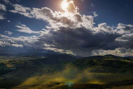 Mysterious mountain landscape with storm clouds hills and sun rays. Beautiful sky. Green grass on hills shimmers in the sunlight. Photo with tinting. Wallpaper for desktop or smartphone.の写真素材