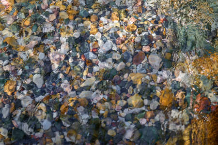 Rocky bottom of mountain stream, close-up. Colorful stones under clear water. Beautiful distortion background. Natural mosaic of small stones. Image for ceramic tile design, bathrooms.の写真素材