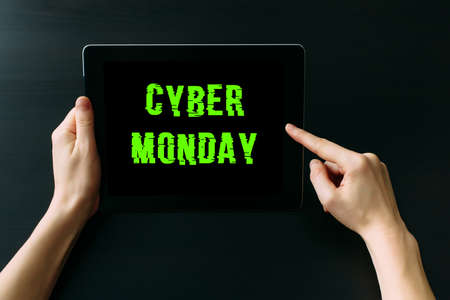 Women's hands holding tablet computer with inscription on screen against black wooden table, close up. Cyber monday concept.の写真素材