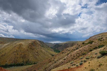 Fantastic deserted landscape. Multi-colored mountains against the sky covered by clouds with sun rays. Red and brown hills. Altai Republic, Siberia, Russia.の写真素材