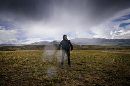 Strange man in black hood and gas mask on the background of mountains, around smoke, fog and radioactive fallout. Concept of environmental pollution, chemical disaster. Ecological catastrophe.の写真素材