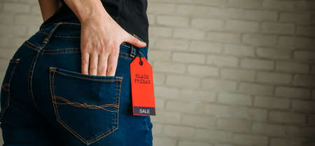 Cropped view slim woman in jeans with label black friday, copy space. Female hands in the back pocket of blue denim pants, close up.の写真素材