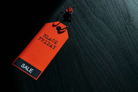 Concept image of label with inscription on dark wooden background, combination of light and shadow. Red tag Black Friday, close-up, copy space.の写真素材