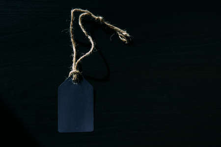 Concept of Black Friday. Empty label on a rope with space for text on black wooden background in sunlight.の写真素材