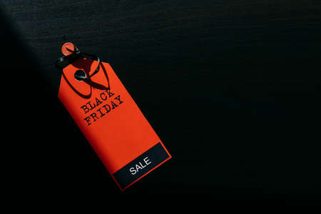 Concept image of label with inscription on dark wooden background, combination of light and shadow. Red tag Black Friday, close-up, copy space.の写真素材