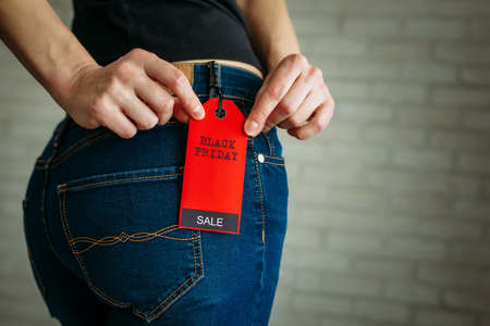 Woman tries on clothes and points to the Black Friday tag. Back view of a slender female butts in blue jeans. Shopping concept, seasonal discounts. Advertising sign.の写真素材
