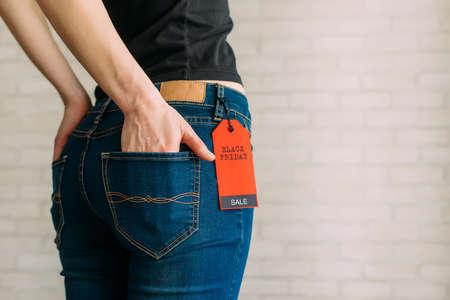 Cropped view slim woman in jeans with label black friday, copy space. Female hands in the back pocket of blue denim pants, close up.の写真素材