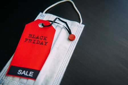 Red tag with the inscription Black Friday on the background of medical mask. Sales in the context of Covid-19 pandemic. Concept of safe shopping.の写真素材