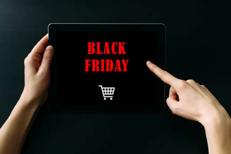 Women's hands holding tablet computer with inscription on screen, dark background, close up. Black friday concept.の写真素材