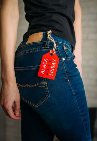 Close up vertical image of sexual woman wearing blue casual denim pants on gray brick background in the mall. Red tag black Friday on jeans.の写真素材