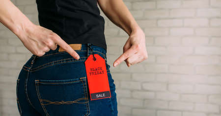 Woman tries on clothes and points to the Black Friday tag. Back view of a slender female butts in blue jeans. Shopping concept, seasonal discounts. Advertising sign.の写真素材
