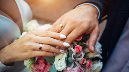 Hands of the bride and groom on the background of wedding bouquet, top view, blurred background. Gold rings on the fingers of newlyweds, close-up.の写真素材