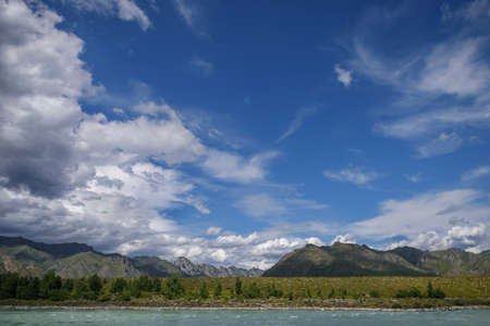Majestic Katun river surrounded by rocky mountains, wooded banks against a blue sky with white clouds. Beautiful natural landscape.の写真素材