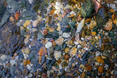 Rocky bottom of mountain stream, close-up. Colorful stones under clear water. Beautiful distortion background. Natural mosaic of small stones. Image for ceramic tile design, bathrooms.の写真素材