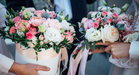 Delicate compositions of fresh flowers in the hands of newlyweds, close-up. Hands of the bride and groom with wedding bouquets of white and pink roses.の写真素材