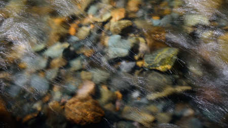 Rocky bottom of mountain river through the clear water, selective focus, blurring the image. Cristal water in the stream shimmers in sunlight. Stone background.の写真素材