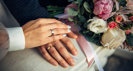 Hands of the bride and groom, wedding bouquet, top view. Gold rings on the fingers of the newlyweds, close-up.の写真素材