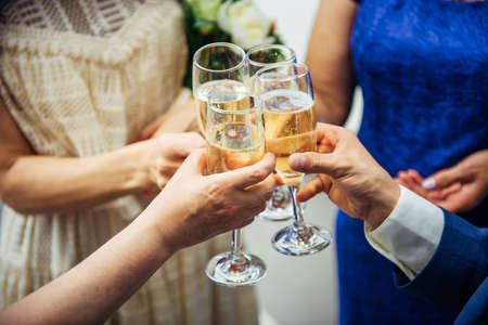 Guests and relatives of different ages at the wedding raise their glasses with festive champagne. Hands with drinks close-up. Marriage celebration, congratulations.の写真素材