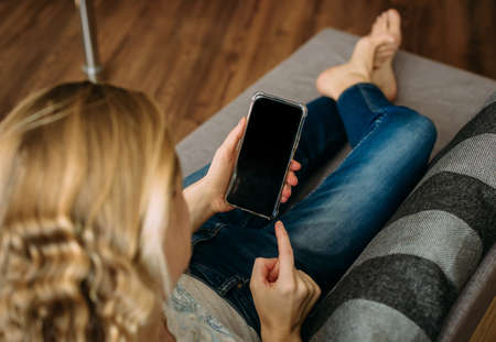 Smartphone with blank screen in hands of young girl on the couch at home.の写真素材