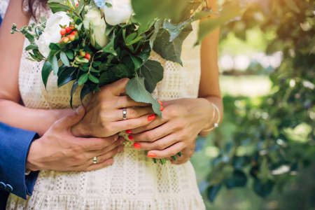 Hands of the bride and groom with wedding rings, bouquet of fresh flowers, vintage lace dress. Husband hugs his wife. Concept of marriage, love, and family life.の写真素材