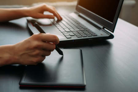 Female designer illustrator working with graphic tablet in modern office. Side view creative artist's hands drawing on digital tablet with pen, close up, black background.の写真素材