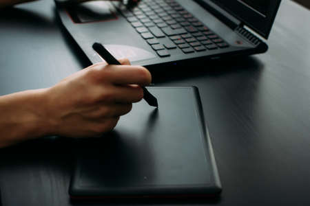 Female designer illustrator working with graphic tablet in modern office. Side view creative artist's hands drawing on digital tablet with pen, close up, black background.の写真素材