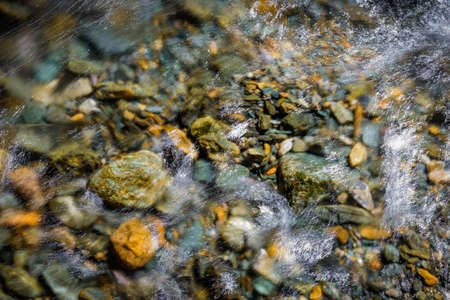 Rocky bottom of mountain river through the clear water, selective focus, blurring the image. Cristal water in the stream shimmers in sunlight. Stone background.の写真素材