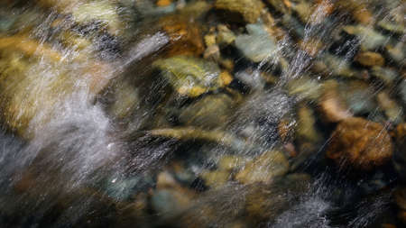 Rocky bottom of mountain river through the clear water, selective focus, blurring the image. Cristal water in the stream shimmers in sunlight. Stone background.の写真素材