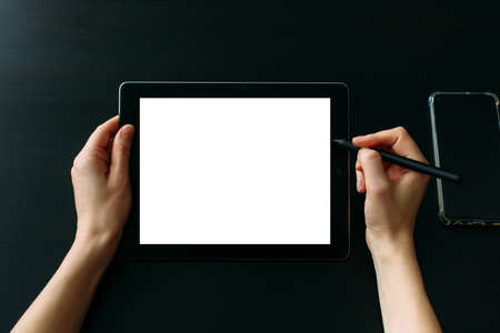 Graphic designer's hands working on tablet with digital pen, close up. Empty white screen, black background.の写真素材