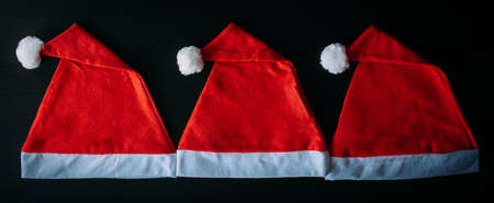 Red Santa Claus hats on black table, top view, close up. Christmas background. New year concept.の写真素材