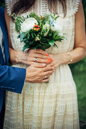 Hands of the bride and groom with wedding rings, bouquet of fresh flowers, vintage lace dress. Concept of marriage, love, family life.の写真素材